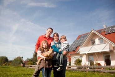Happy,Family,Standing,In,Front,Of,House,With,Solar,Panels